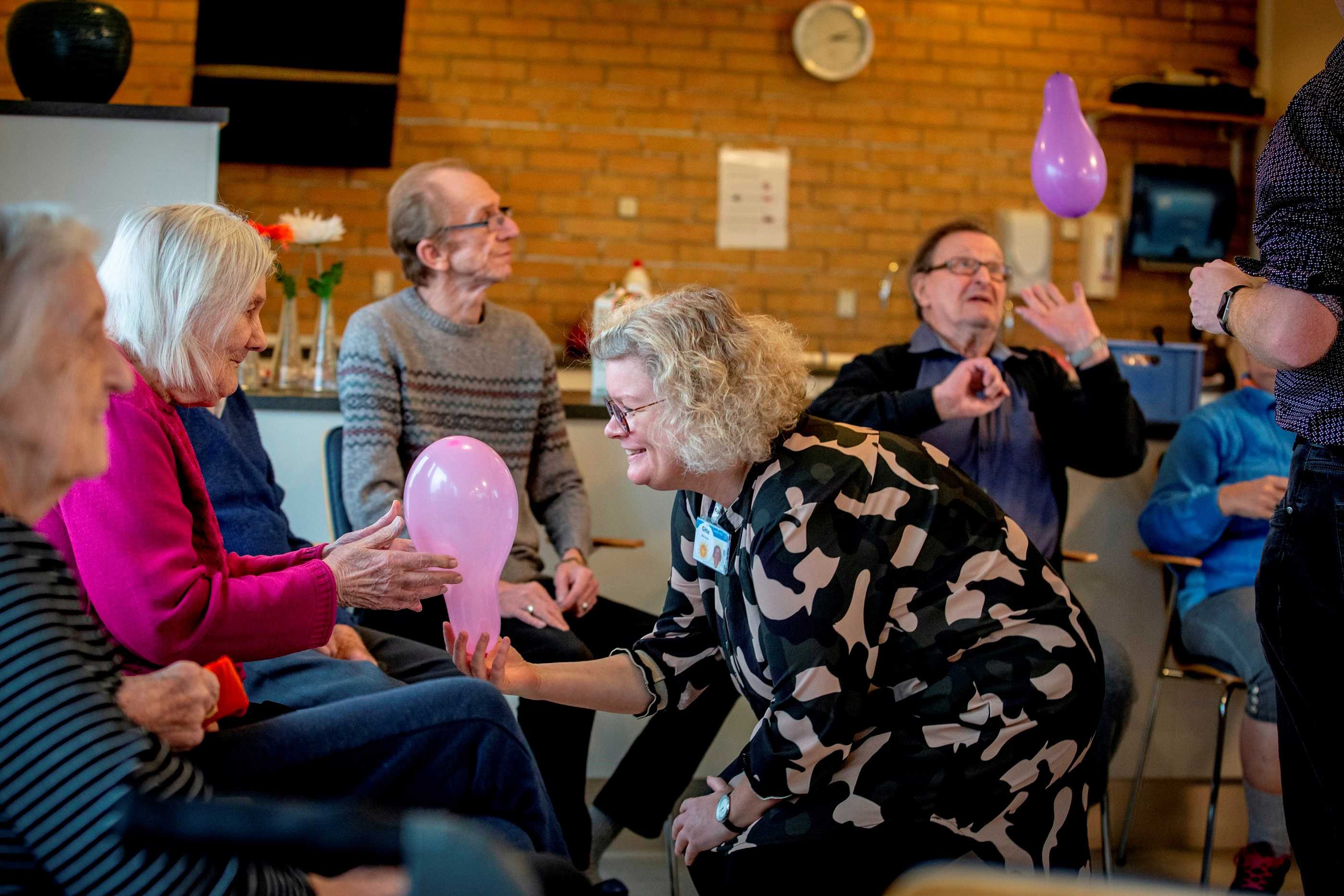 Ballondans i Birke-Bo, hvor kvinde giver en der sidder ned en ballon.