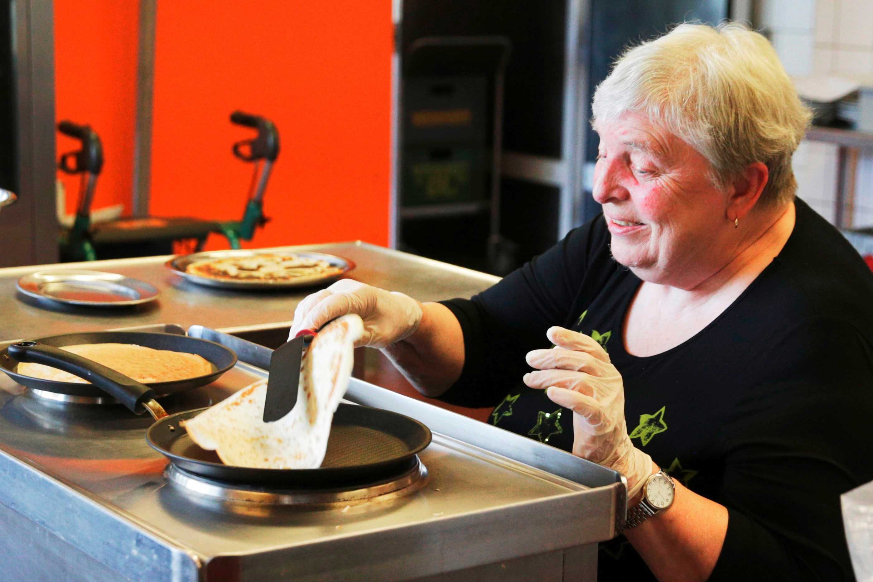 Siddende kvinde laver pandekager i aktiviteten på Bakkegården