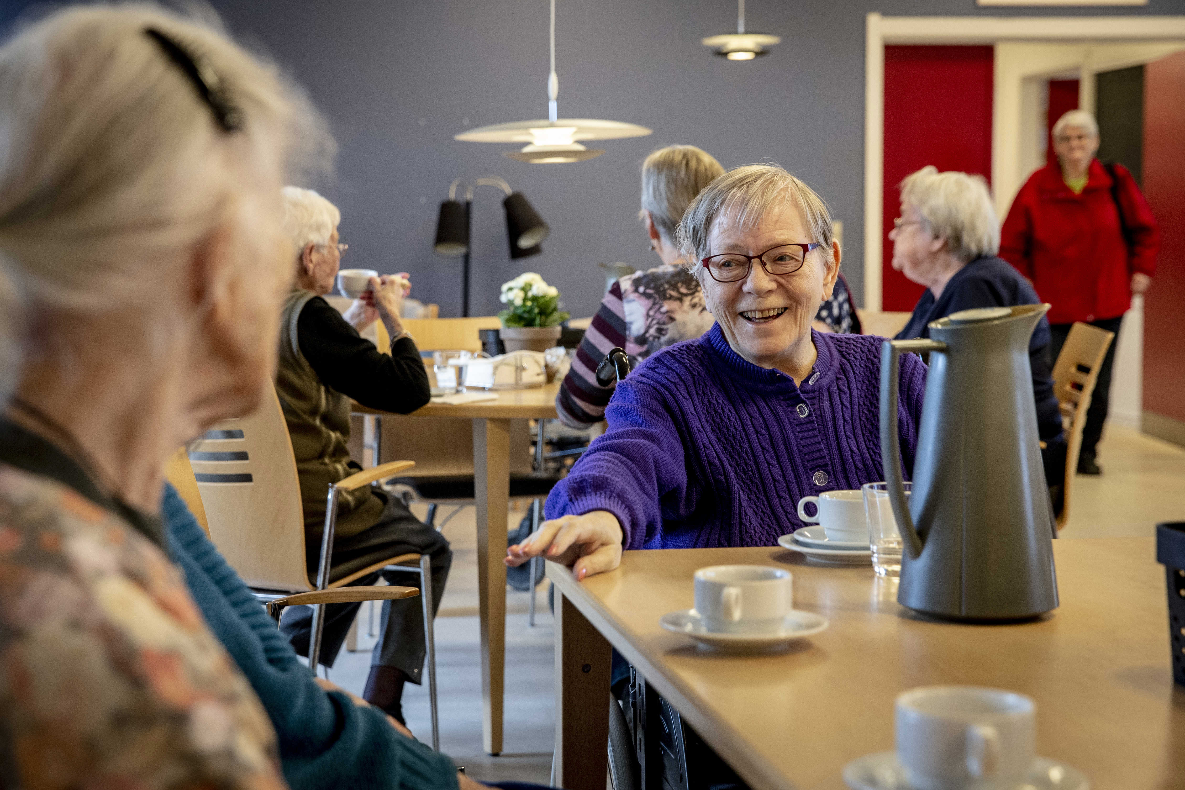 Kvinde sidder og smiler til dem der er ved hendes side ved kaffebordet