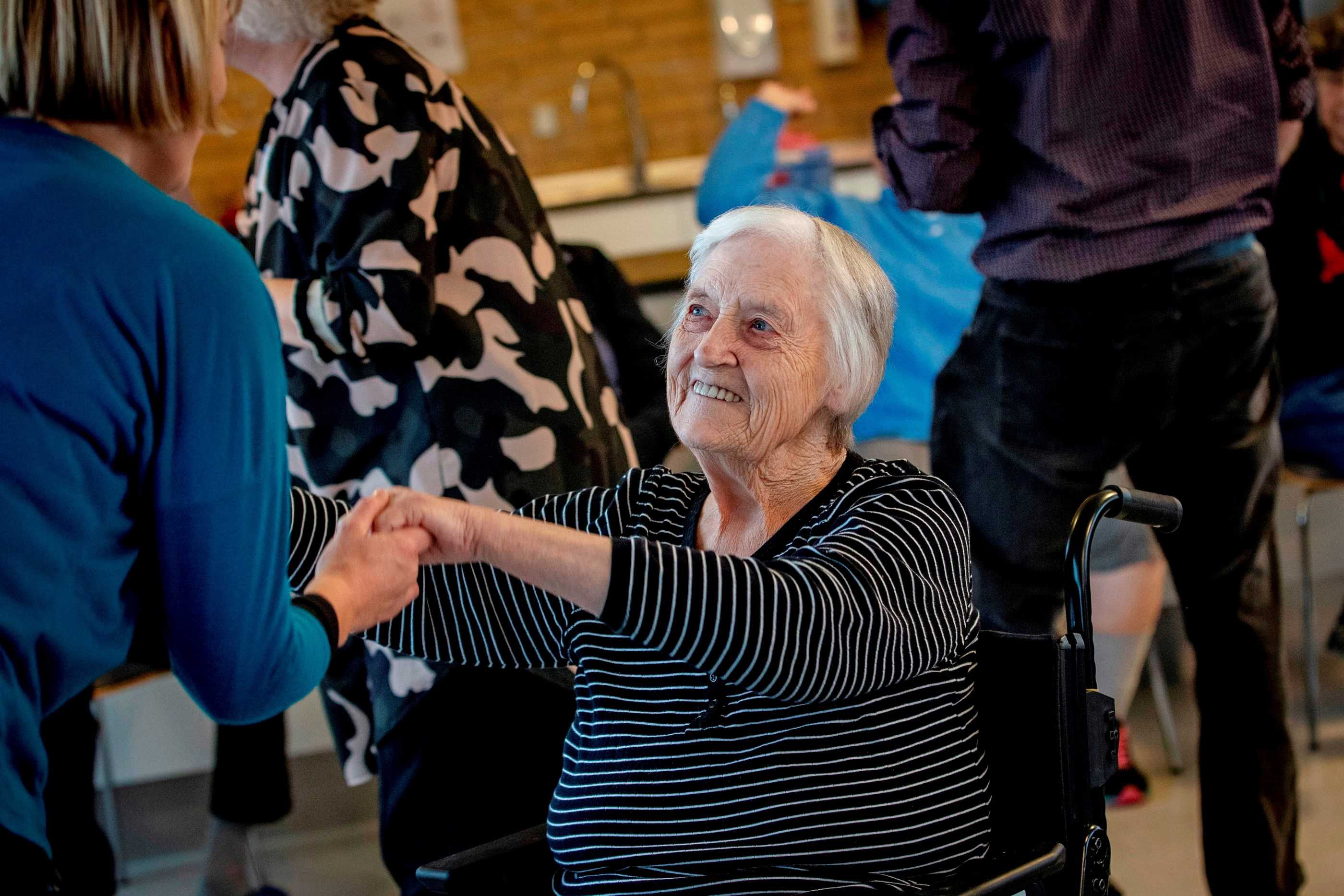 Kvinde i kørestol danser med et personale og smiler optil hende